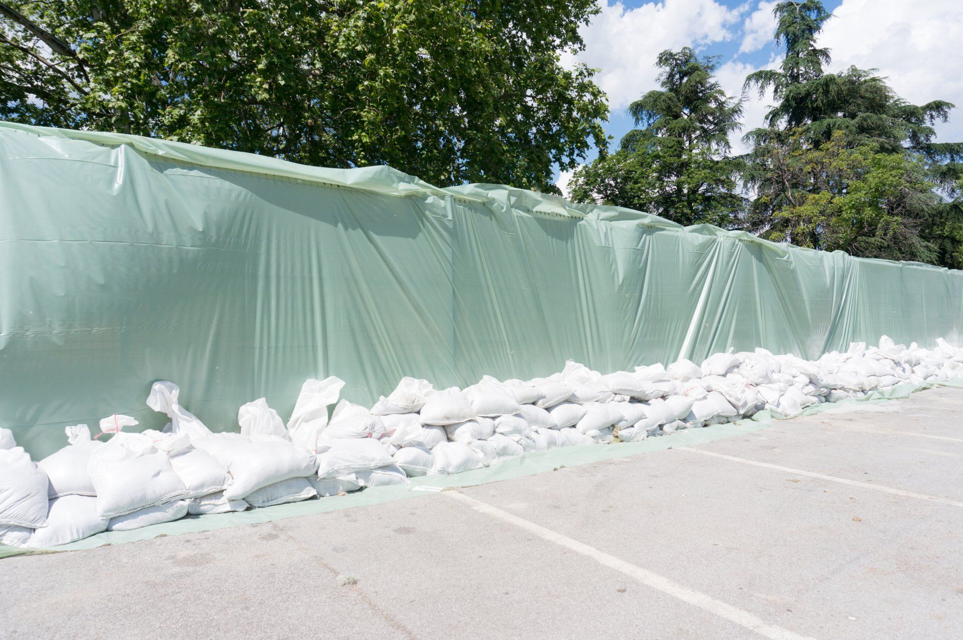 Green tarp-covered wall reinforced with sandbags, likely for flood protection, in a parking lot. Cover-Tech Emergency Relief Products.