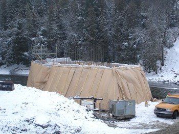 A yellow truck is parked in front of a building covered in tarps