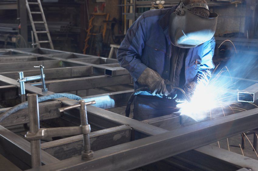 A man is welding a piece of metal in a factory.