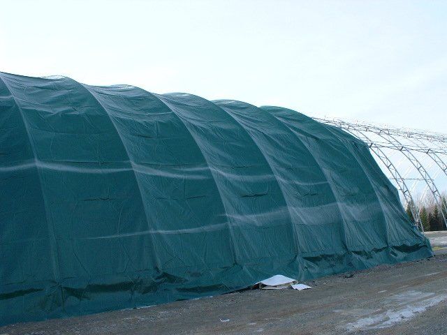 A large green tarp is covering a building in a field.