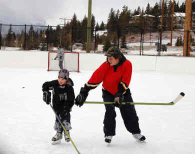 A man is teaching a young boy how to play hockey on a rink.