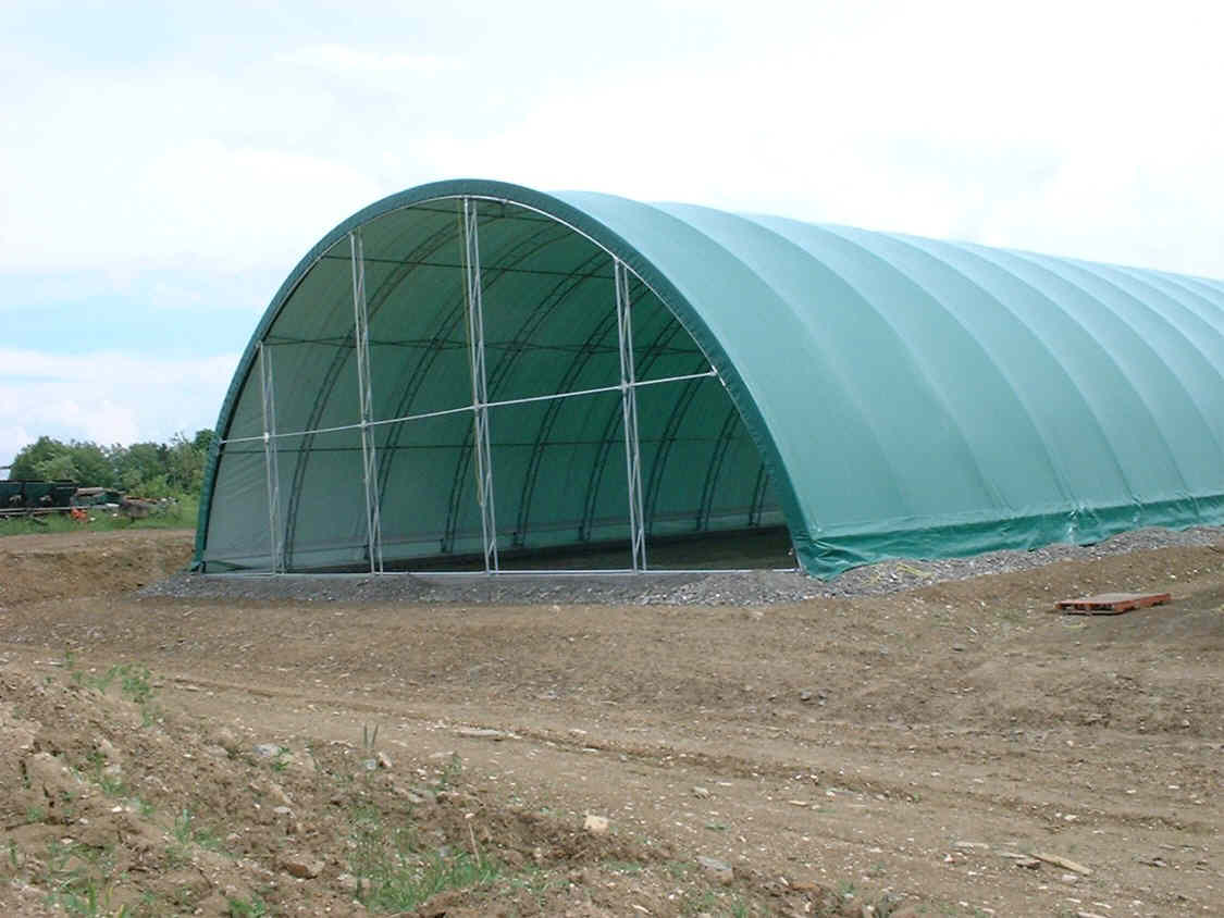 A large green tent is sitting in the middle of a dirt field.