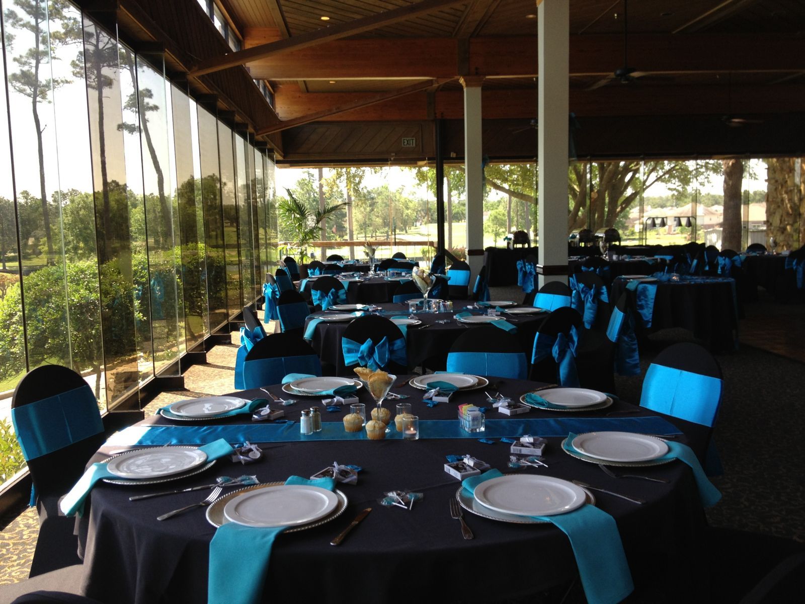 Formal dining room set for an event with black tablecloths, teal accents, and outdoor views.