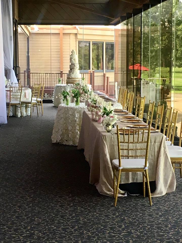 Wedding reception: long tables with gold chairs set for guests, overlooking a green landscape.