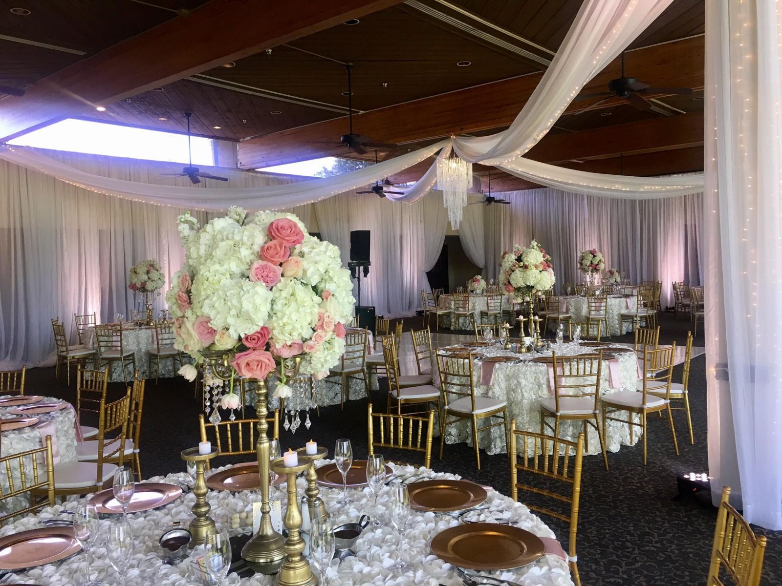 Elegant wedding reception. Round tables with gold chairs, floral centerpieces, and white draping.