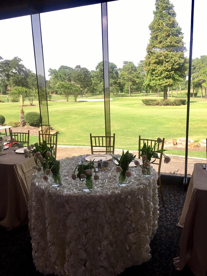 A round table with white floral tablecloth, tulips, and golf course view.