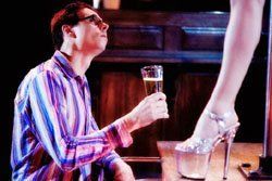 A man is kneeling down in front of a pole dancer holding a glass of champagne.