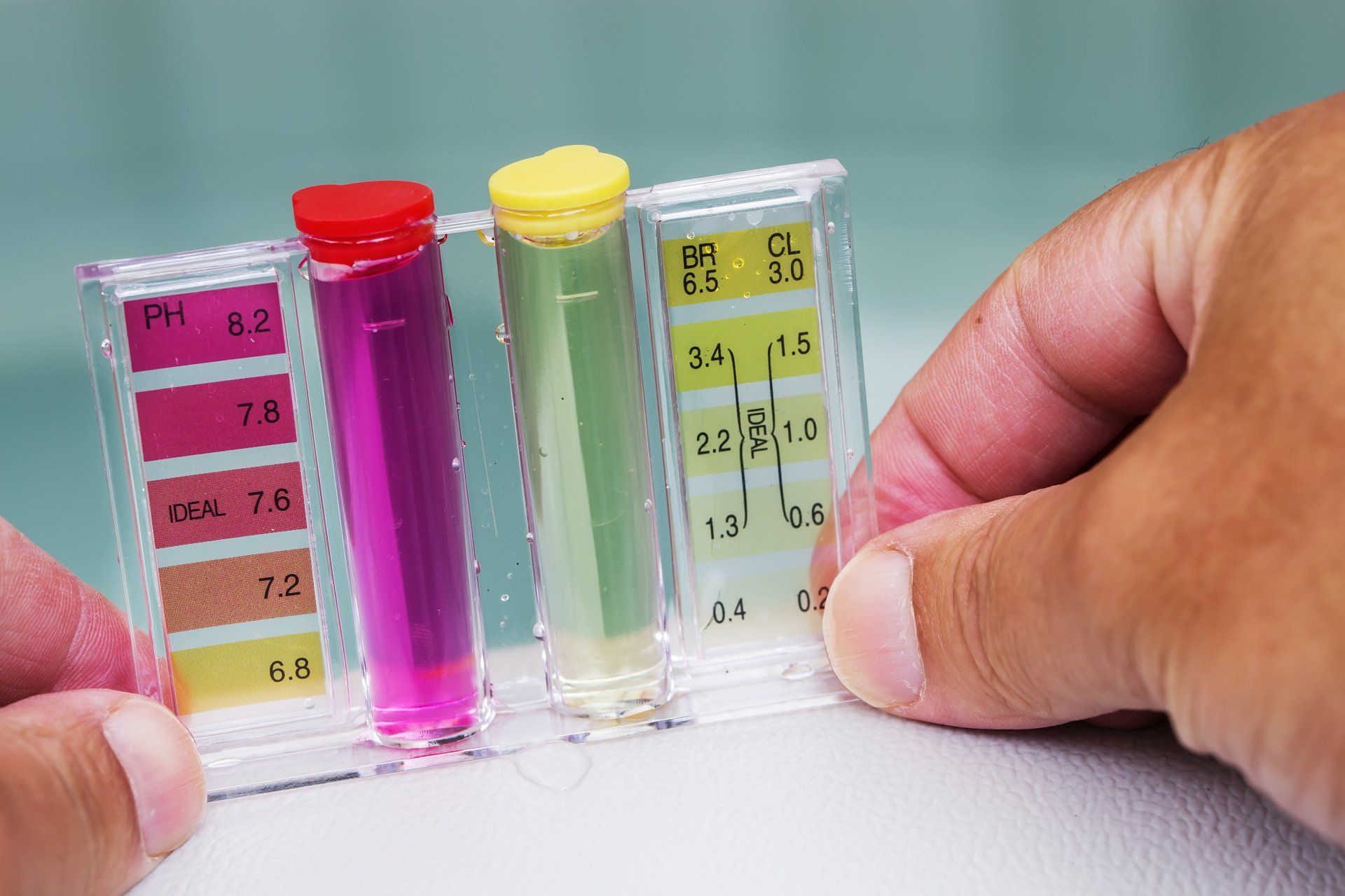 Hands holding a pool water test kit; pink, green, and yellow liquids show the levels of chemicals.