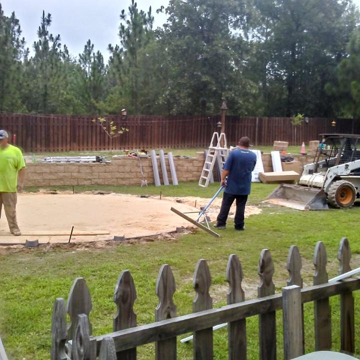 Construction workers building a pool in a backyard, using equipment and tools.