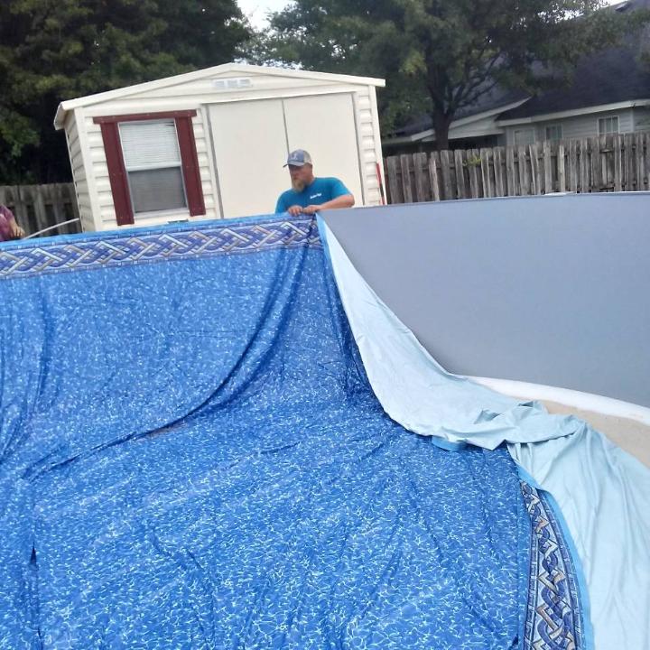 Man installing blue pool liner, shed in background.