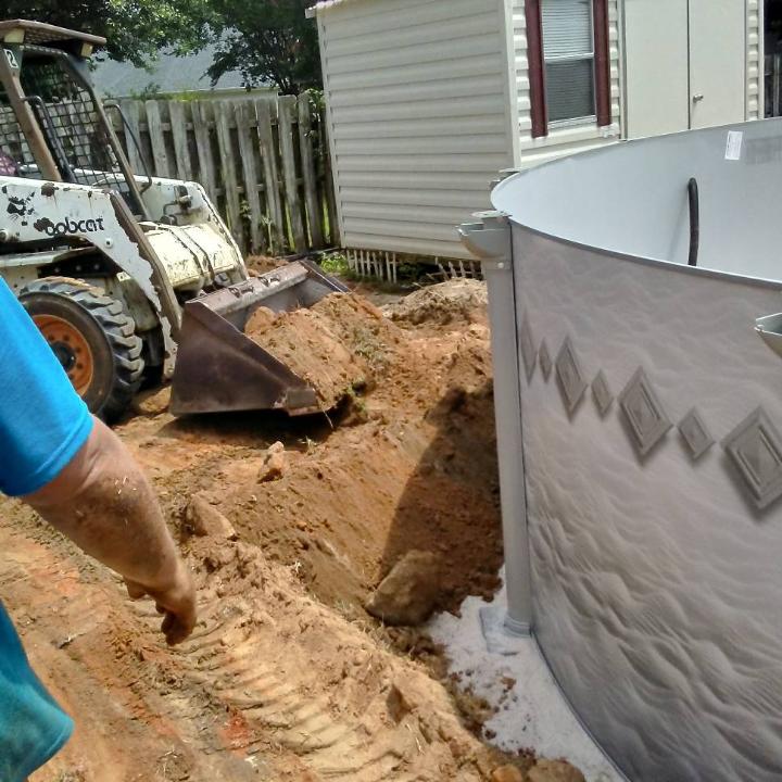 Bobcat excavator digging near a partially constructed above-ground pool.