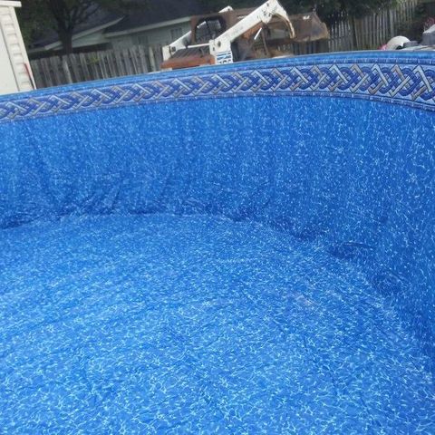Inside of a blue above-ground pool, top edge with braided pattern. Construction vehicle visible in background.