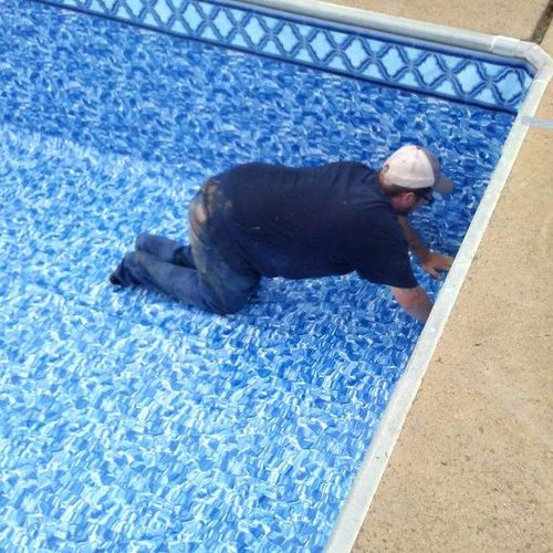 Person installing a blue patterned pool liner in an empty pool.