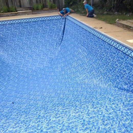 Two people installing a blue patterned pool liner into an empty pool.