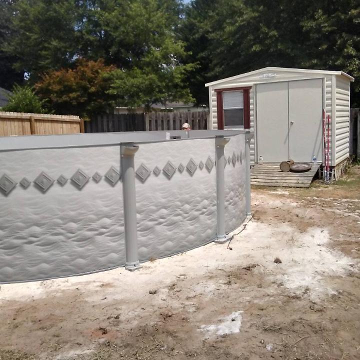 Above-ground pool in a yard next to a storage shed with a wooden fence.