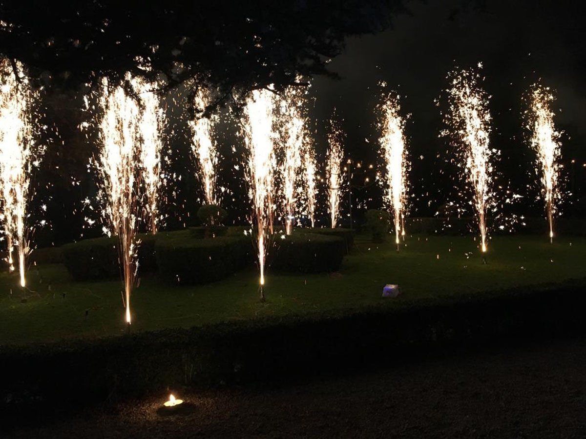 Fontane di fuochi d'artificio bianchi eruttano su un prato buio di notte.