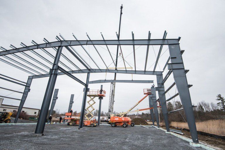 Steel frame of a building under construction, with cranes and lift platforms. Gray skies.