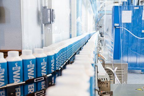 Bottles of blue and white liquid product on an industrial conveyor belt.