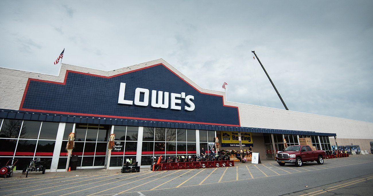 Exterior of a Lowe's store with a dark blue sign, flags, and a red truck parked outside.