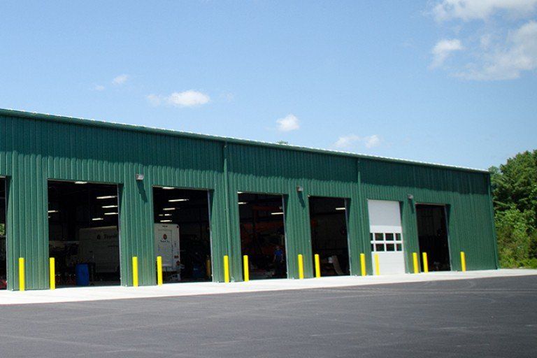 Green metal building with open garage doors and yellow safety poles.