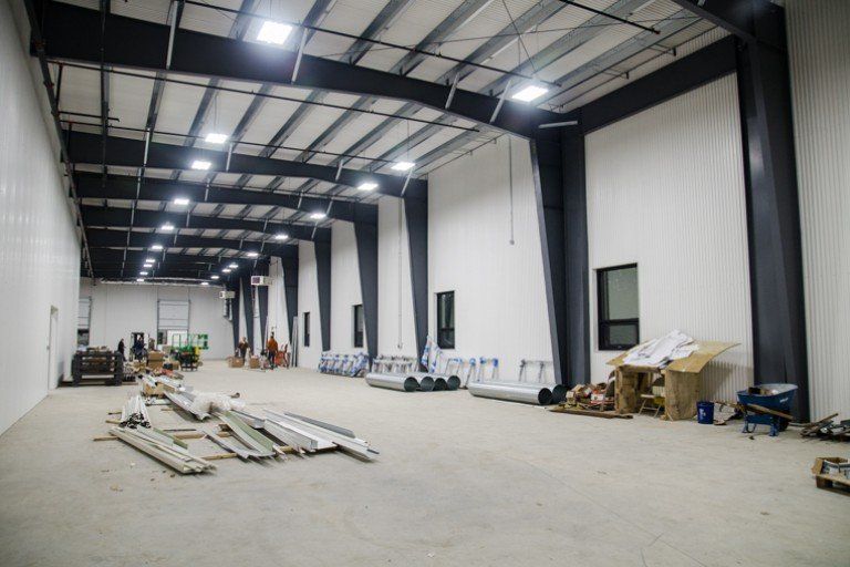 Large, empty warehouse interior with metal beams, white walls, and scattered construction materials.
