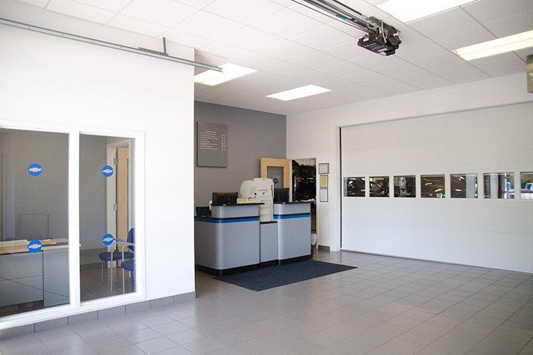 Reception area with front desk, garage door, and windows. Interior is painted white, with gray accents.