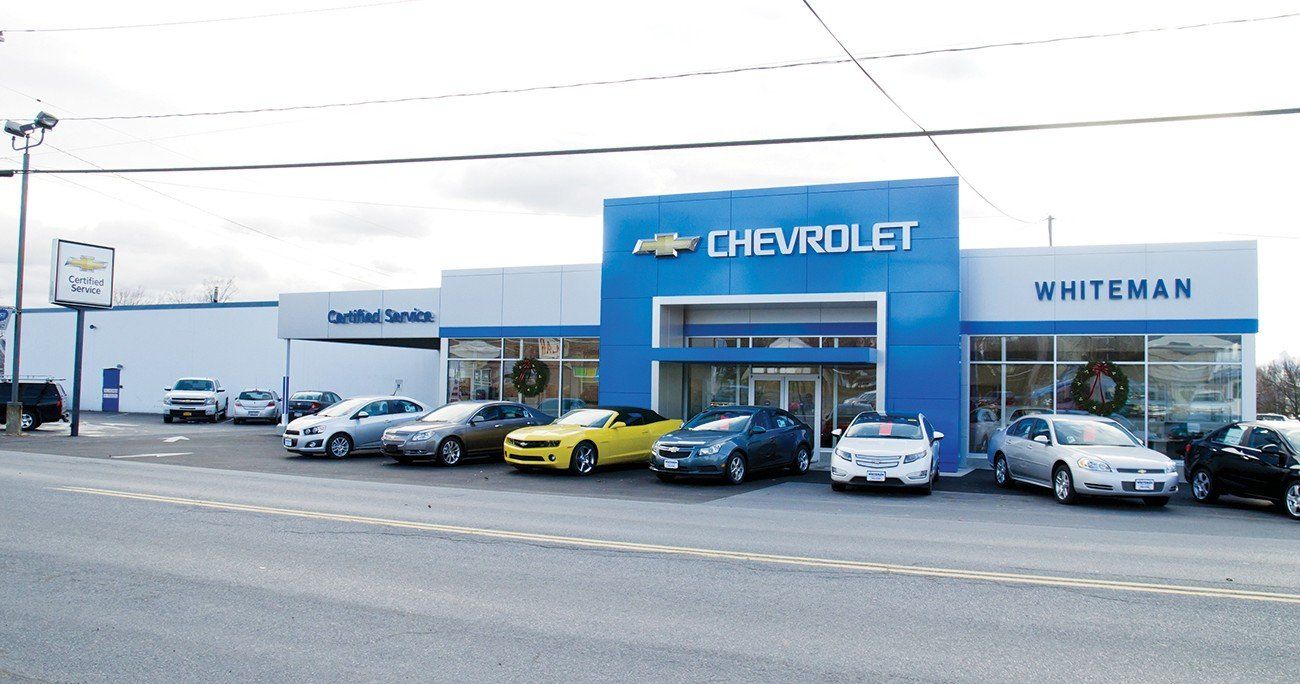 Chevrolet car dealership with cars on display; blue and white building, sunny day.
