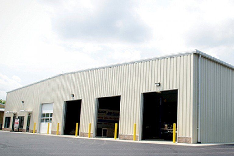 Light beige metal building with three large garage bays and an open door.