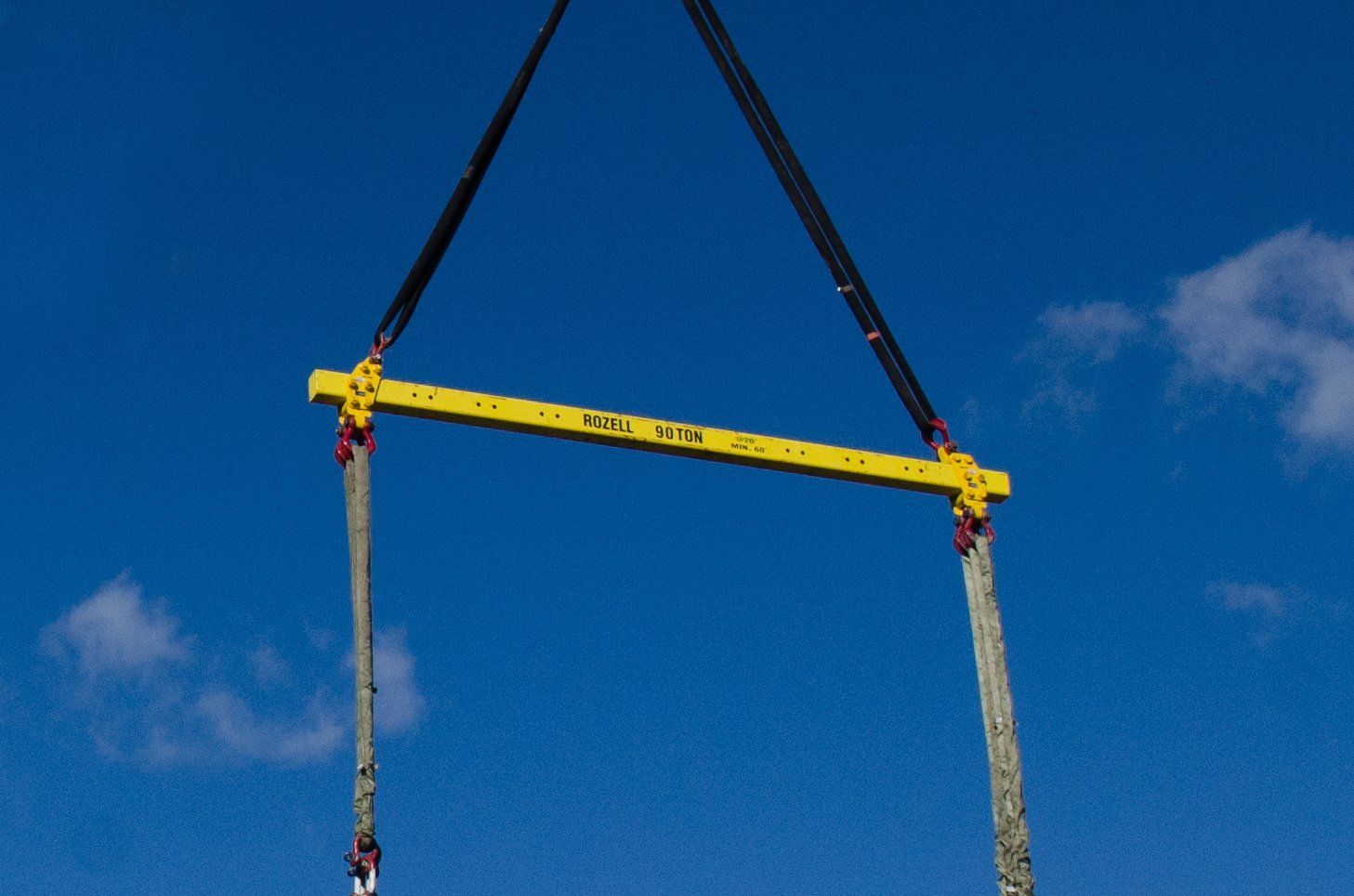 Yellow spreader bar suspended by cables against a blue sky.