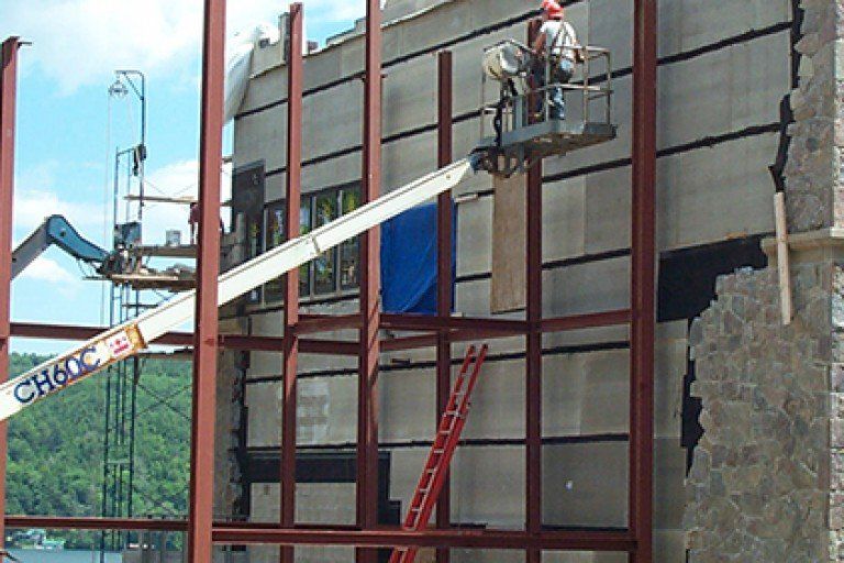 Construction worker in lift basket working on building exterior. Steel framework visible.