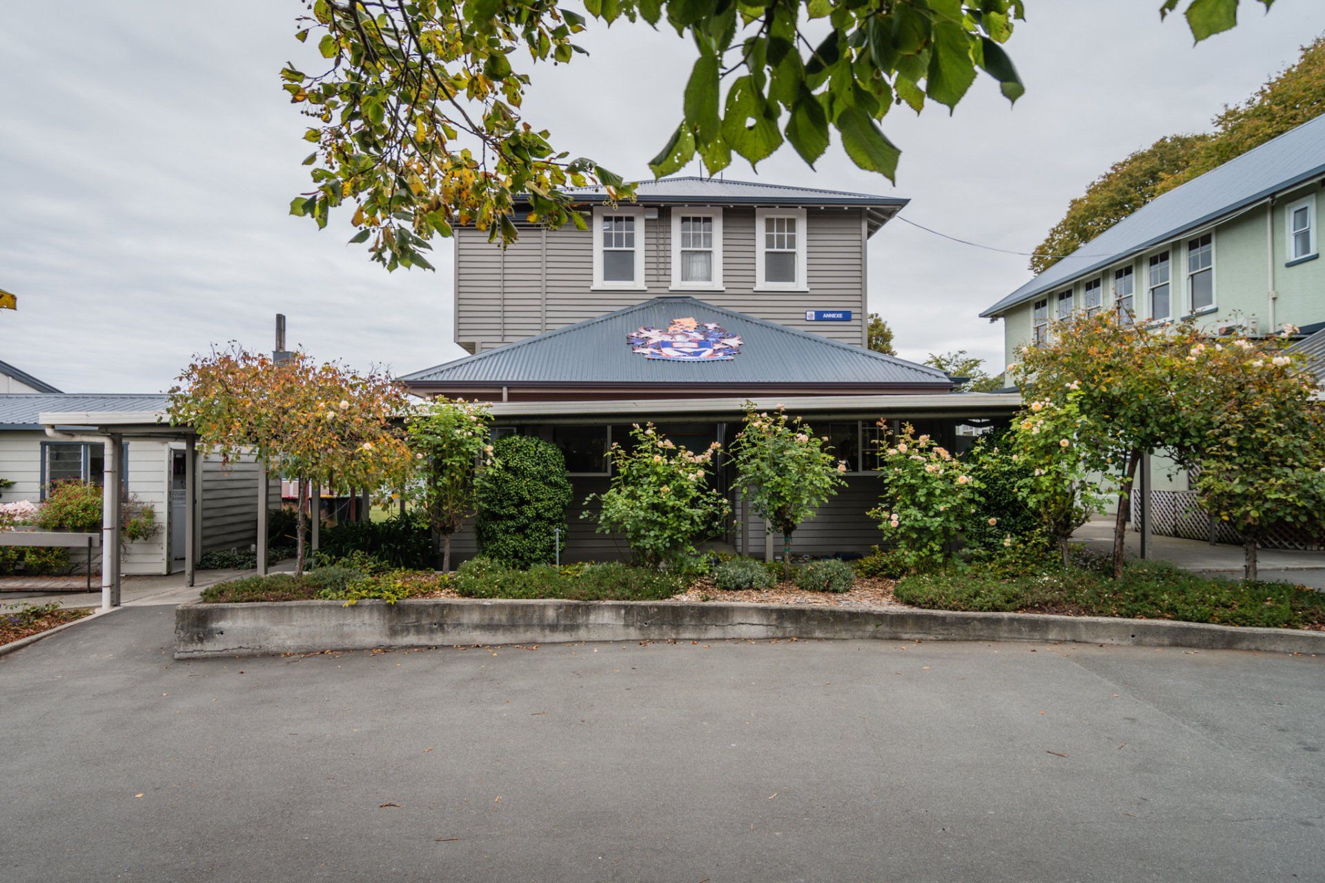 A large house with a flag on the roof is surrounded by trees and bushes.
