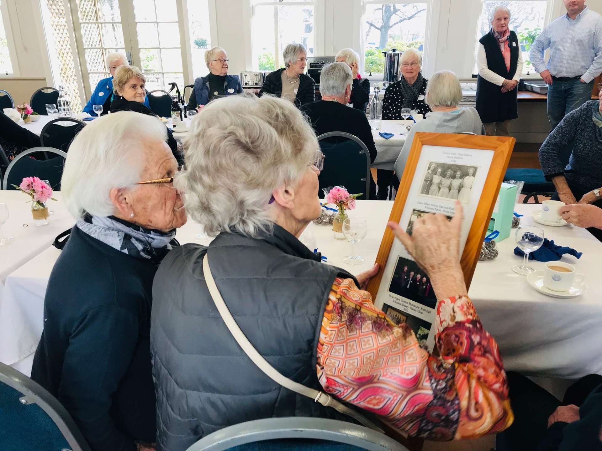 A woman is sitting at a table holding a framed picture.