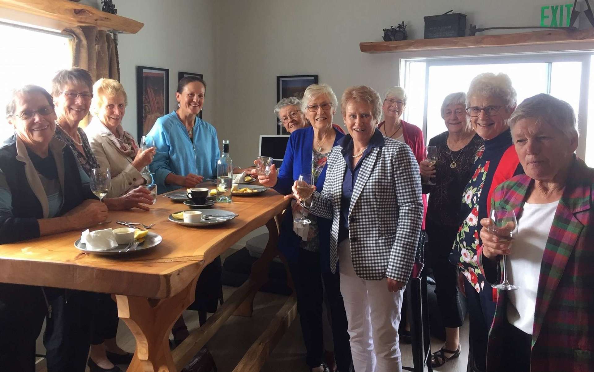 A group of women are standing around a long wooden table.