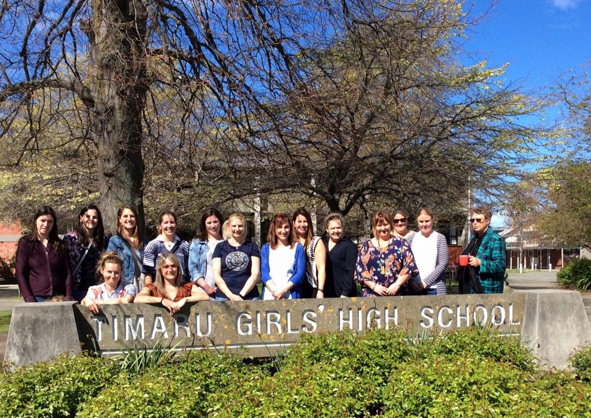 A group of people are posing for a picture in front of a sign for timaru girls ' high school.