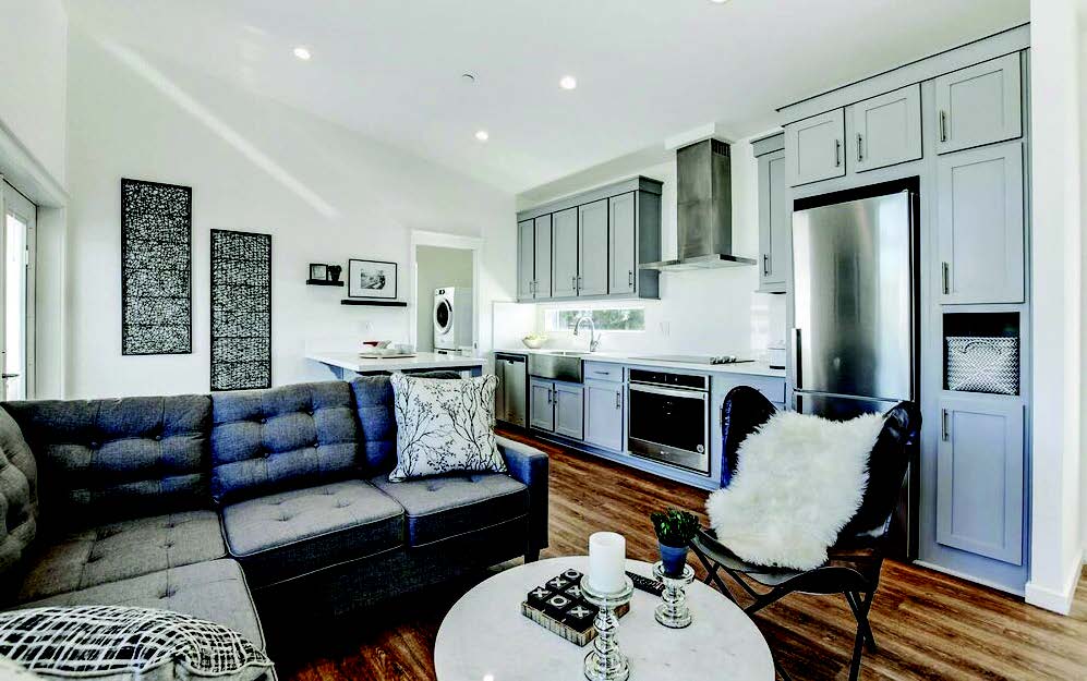 Interior of ADU with cozy living space with gray cabinets, sofa, and kitchen appliances; hardwood floors.