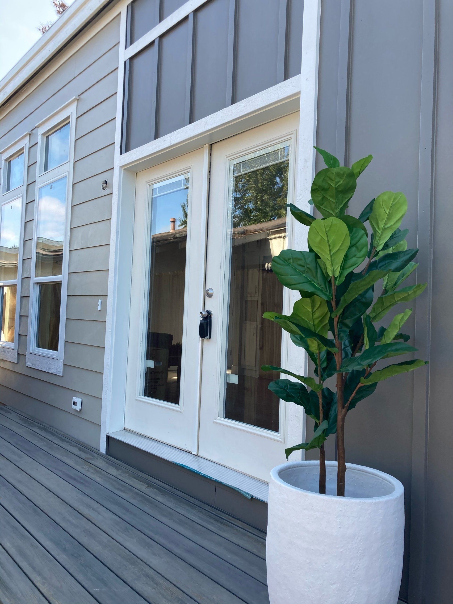 Perpetual Homes ADU: White French doors and windows on a gray building, with a potted fiddle-leaf fig on a wooden deck.