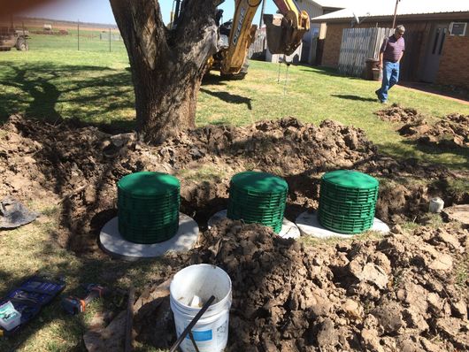 Three green septic tank covers in a muddy yard near a tree and construction equipment