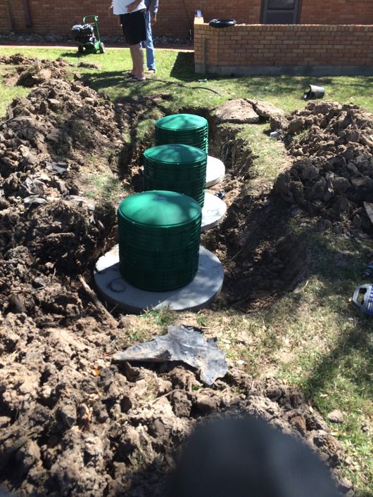 Green utility tanks in a muddy trench at a construction site, with workers in the background.