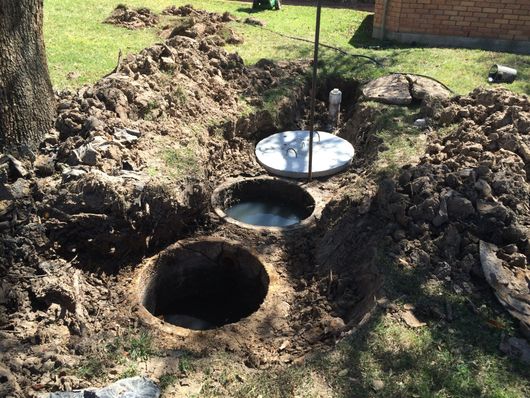 Three large holes dug in a grassy yard beside a metal cover and shovel.