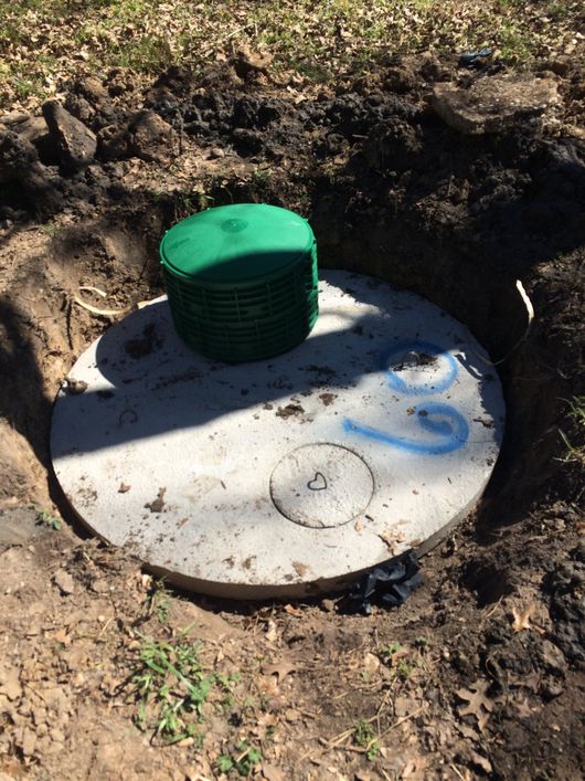 Green utility cap on a round concrete cover in a dirt excavation hole.