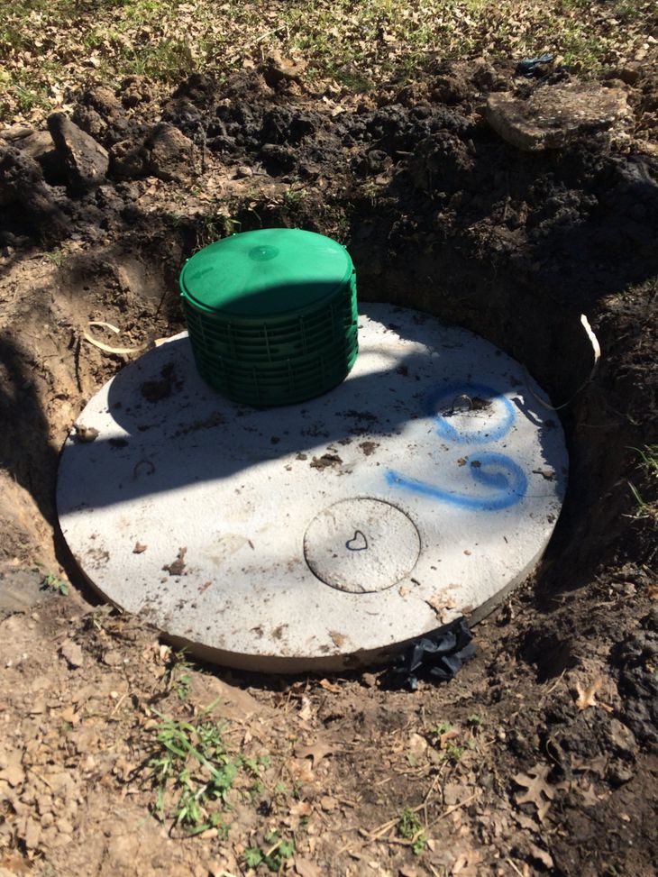 White circular utility cover with green cap set in dirt excavation trench
