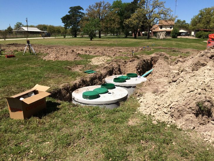 Excavated trench with white utility covers and green lids beside a dirt pile in a grassy field