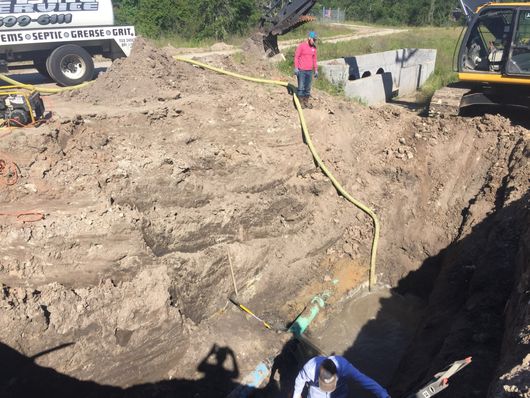 Large muddy excavation site with workers, heavy equipment, and a hose on a dirt slope