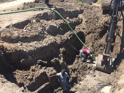 Workers digging large trenches at a construction site with an excavator nearby
