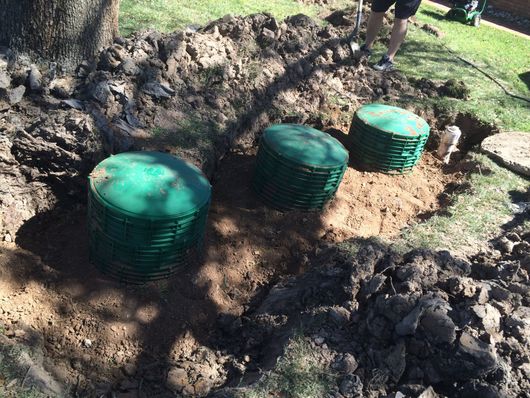 Three green septic tank lids installed in a muddy trench outdoors