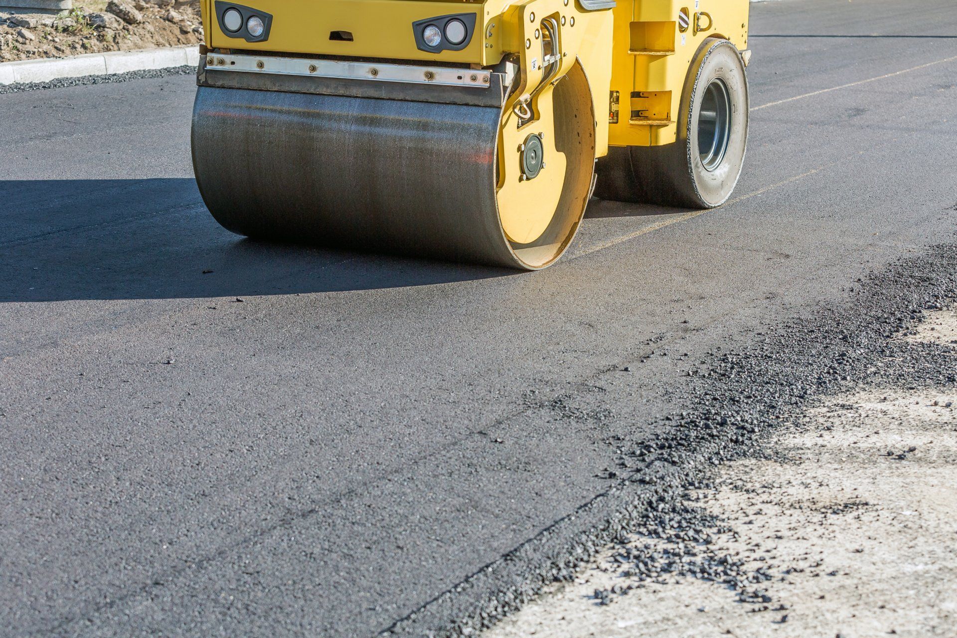 Yellow road roller compacting fresh asphalt on a street construction site