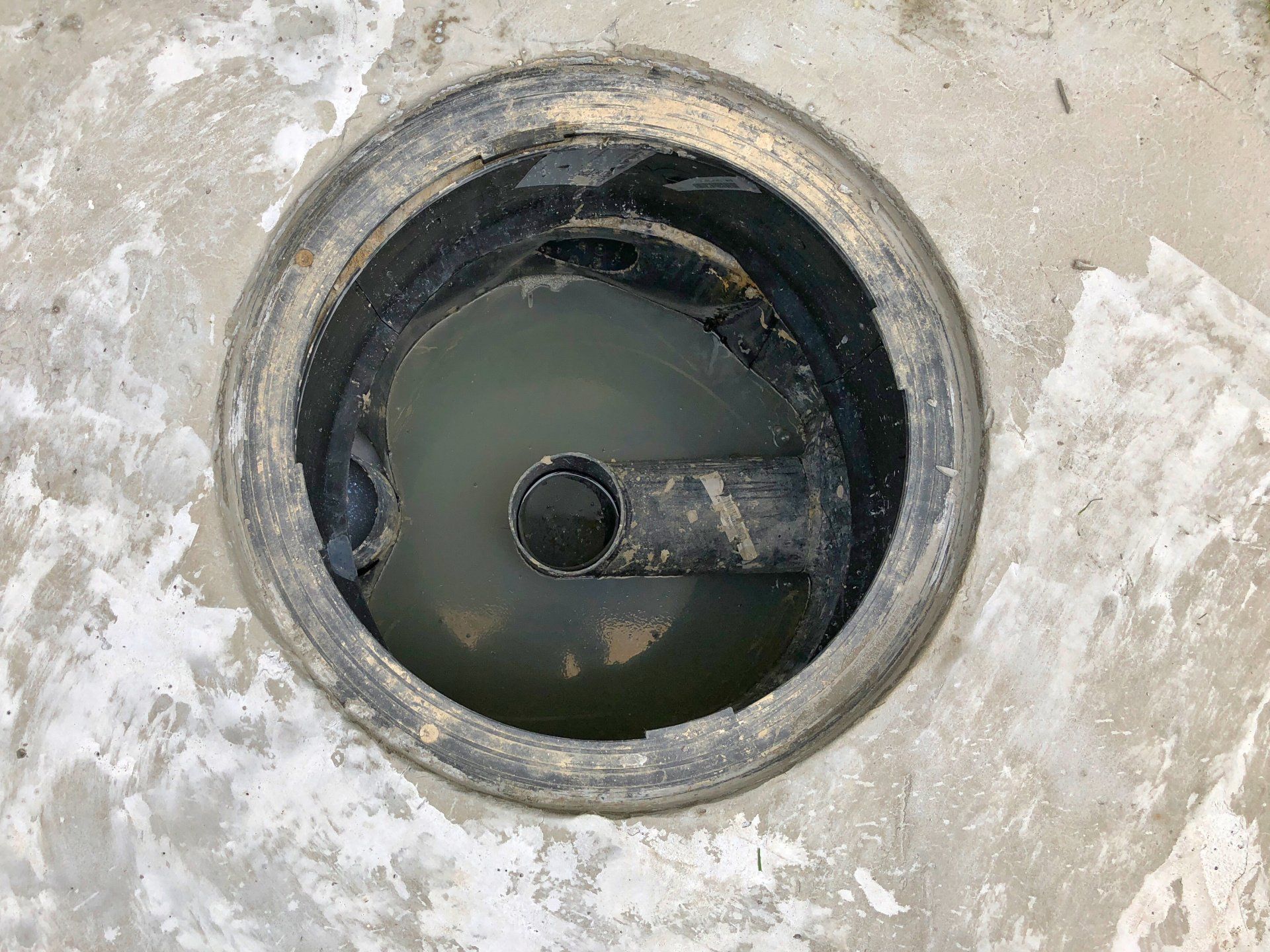 Circular manhole opening with standing water and a dark pipe or valve inside the concrete surface
