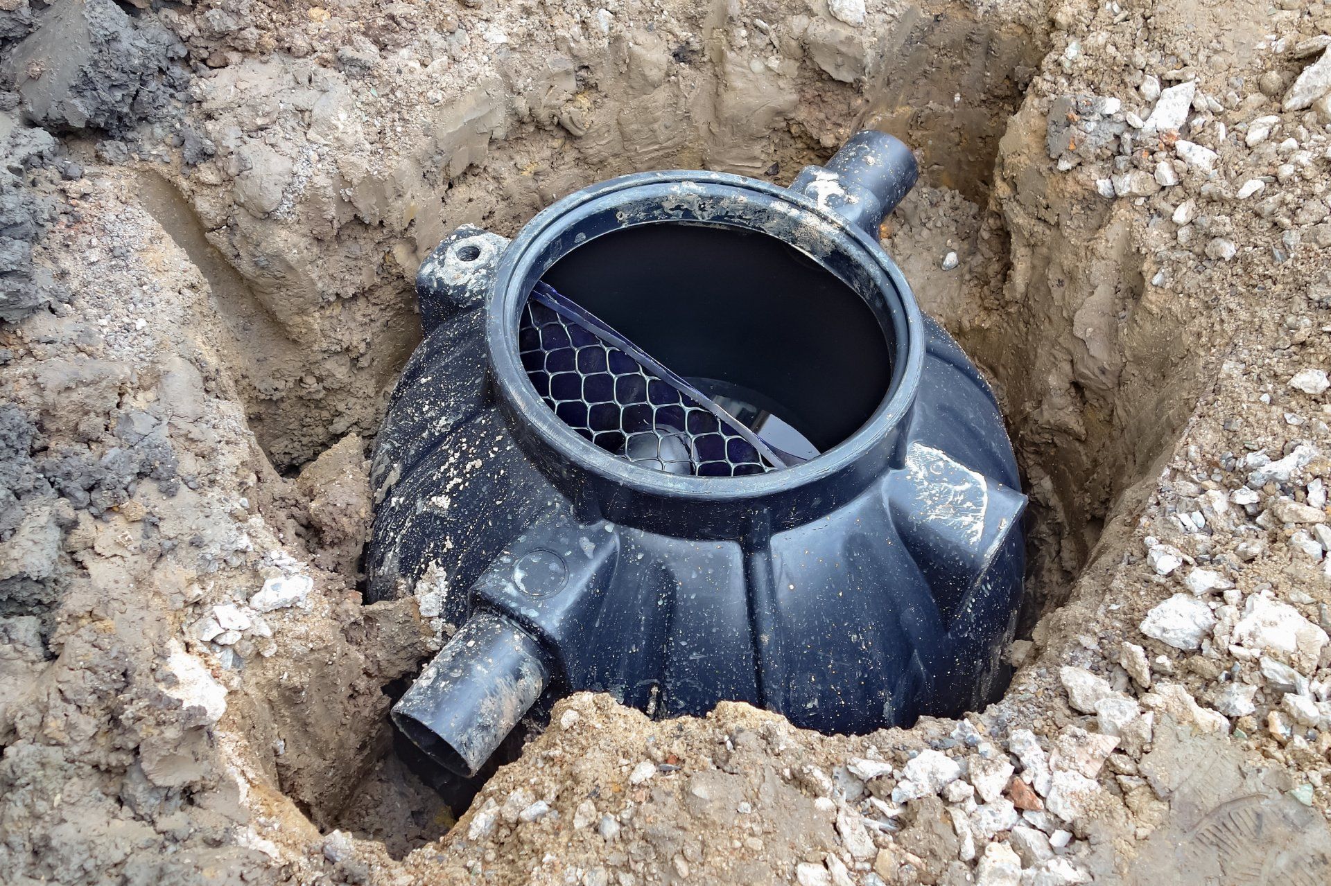Black plastic pipe chamber in a dirt excavation hole with visible inlet and outlet pipes