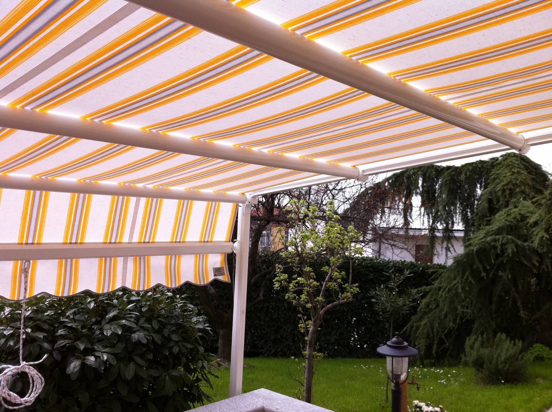 Tenda a capanno a strisce gialle e bianche sopra un patio in giardino.