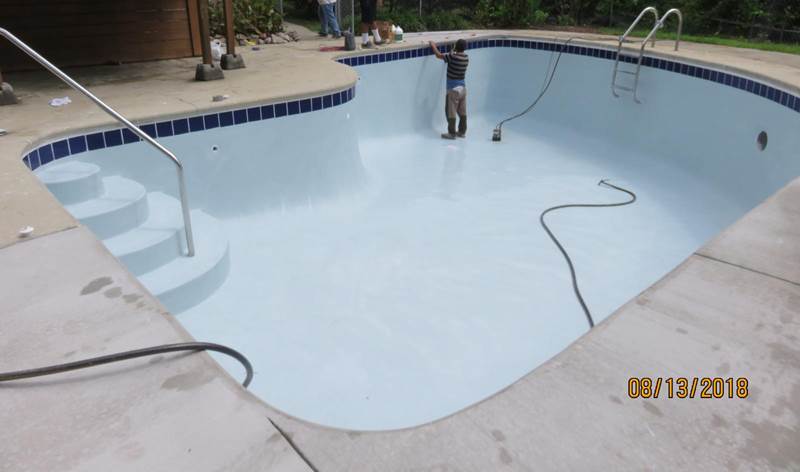 worker standing in empty inground pool after replaster
